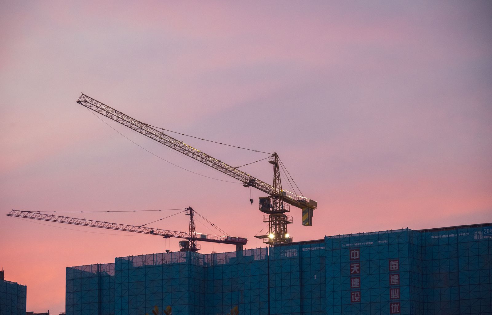 夕暮れの空に複数のタワークレーンが並ぶ大規模建設現場